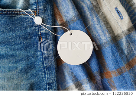 Close-up of a blank round tag attached to blue denim and plaid fabric Close-up of a blank round tag attached to blue denim and plaid fabric 132226830