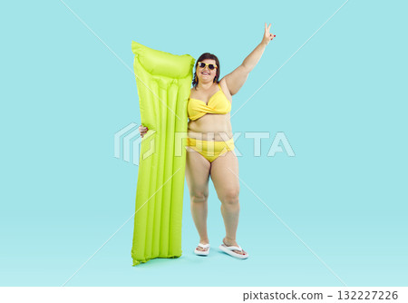 Fat funny woman in bikini holding her inflatable mattress on studio blue background. 132227226