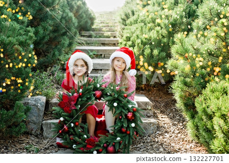 Merry Christmas. Portrait of two happy funny children girls in Santa hat with Christmas wreath. Happy Holidays. Fairy Magic. Happy kids enjoying holiday. Christmas in July 132227701