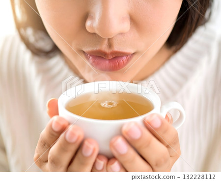 女人的嘴唇輕輕地用雙手捧著一個熱氣騰騰的碗 132228112