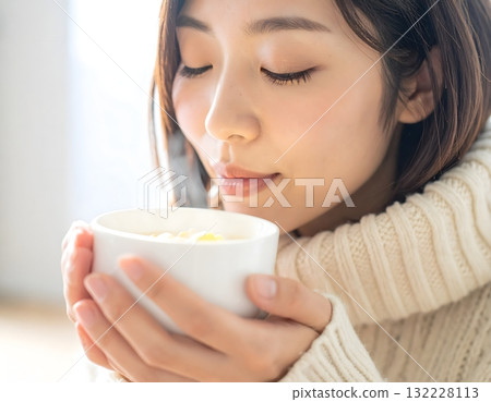 A woman in a warm sweater cools down a hot bowl of soup A woman in a warm sweater cools down a hot bowl of soup 132228113