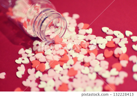 Heart-shaped sugar topping spilling from a small bottle. Cute background decoration. Overflowing feelings. Confectionery ingredients. Heart-shaped sugar topping spilling from a small bottle. Cute background decoration. Overflowing feelings. Confectionery ingredients. 132228413