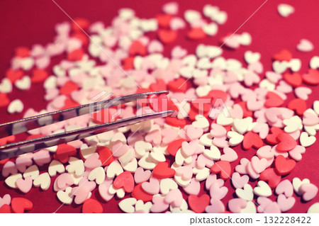 Heart-shaped topping sugar picked with tweezers. Stylish and cute background decoration. Feelings. Confectionery ingredients. Heart-shaped topping sugar picked with tweezers. Stylish and cute background decoration. Feelings. Confectionery ingredients. 132228422