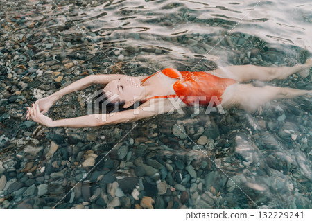 Woman swimming water, serene woman in red swimsuit floating over pebble beach. Woman swimming water, serene woman in red swimsuit floating over pebble beach. 132229241