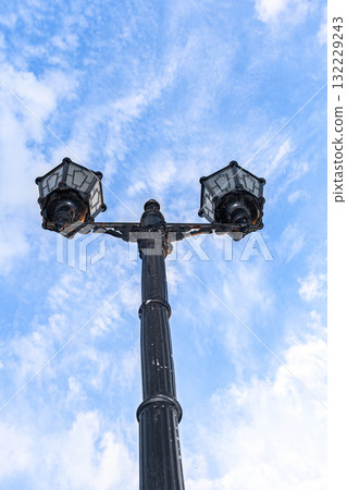 Vintage street lamp with two lanterns against a bright blue sky and fluffy white clouds 132229243
