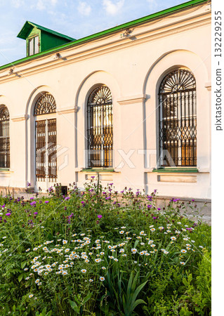 White building with arched windows surrounded by vibrant flowers in a sunny garden setting 132229255