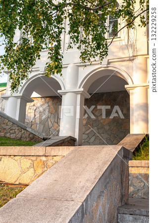 Architectural details of stone steps leading to arched columns under a leafy tree canopy 132229258
