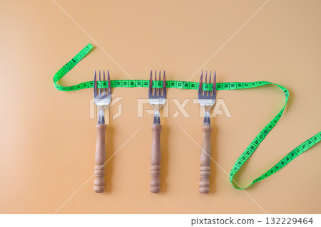 Green measuring tape on three forks.Healthcare concept. Green measuring tape on three forks.Healthcare concept. 132229464