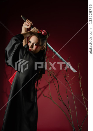 Woman poses elegantly in traditional Japanese dress holding a sword in a studio setting Woman poses elegantly in traditional Japanese dress holding a sword in a studio setting 132229756
