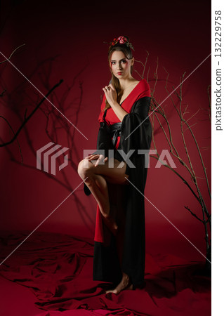 Woman poses gracefully in traditional Japanese dress against a striking red backdrop Woman poses gracefully in traditional Japanese dress against a striking red backdrop 132229758