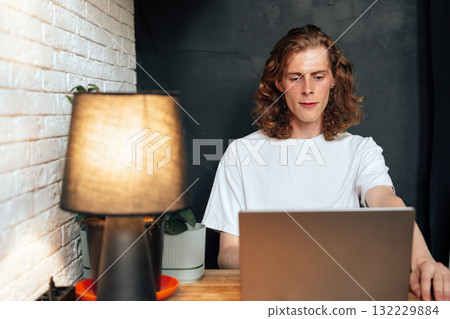 Young man working on laptop at a cozy desk with warm lighting in a modern space 132229884
