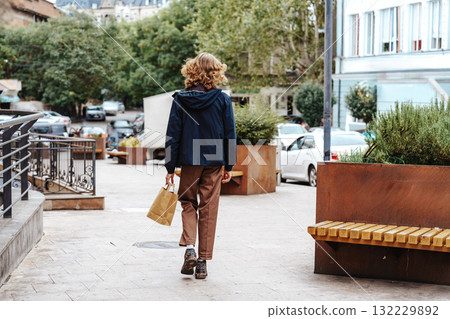 Young person walks through a city street holding a brown paper bag in autumn 132229892