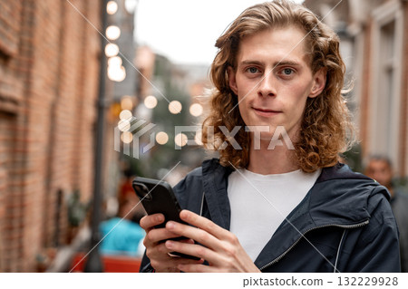 Young man using smartphone in a lively street with warm lights at dusk 132229928
