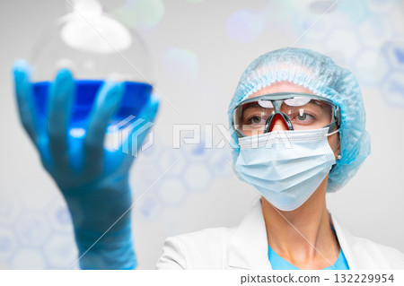 Scientist examines blue liquid in laboratory under bright lights during research experiment 132229954