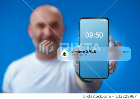 Smartphone shows Christmas sale notification at 09:50 with man smiling in background 132229967