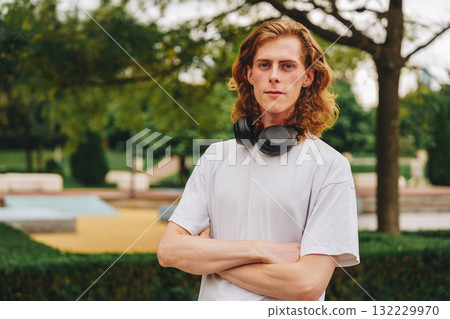 Young man with curly hair poses confidently in a park while wearing headphones 132229970
