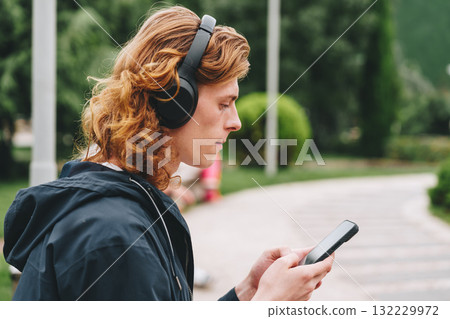 Young person listens to music while using smartphone in a city park setting 132229972
