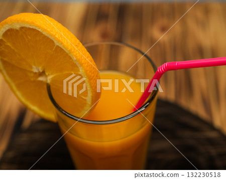 Full glass of orange juice close-up. Fresh orange juice on wooden table in out of focus unidentified restaurant in the morning in summer. Full glass of orange juice close-up. Fresh orange juice on wooden table in out of focus unidentified restaurant in the morning in summer. 132230518