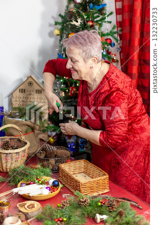 Smiling senior old woman craft. Grandmother make Christmas wreath from pine branches. Home decoration in December. Winter Holiday preparing Smiling senior old woman craft. Grandmother make Christmas wreath from pine branches. Home decoration in December. Winter Holiday preparing 132230733