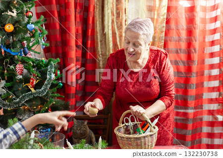 Senior old woman craft. Grandmother make Christmas wreath from spruce branches. Home decoration in December Senior old woman craft. Grandmother make Christmas wreath from spruce branches. Home decoration in December 132230738