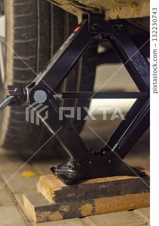 Car Lifted with Scissor Jack During Tire Replacement on Wooden Support Blocks 132230743