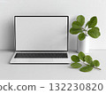 Laptop with blank screen placed on white desk beside green leaves. Clean office decor setup for professional or creative workspace inspiration. 132230820