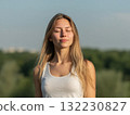 Young girl taking deep breath in nature, surrounded by lush green trees and clear sky. Healthy living and self control shown in peaceful outdoor scene. 132230827