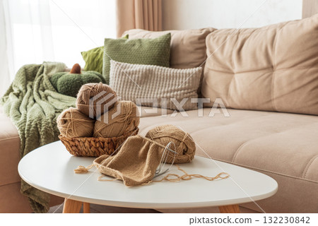 Knitting Basket with Yarn and Needles on White Table in Cozy Interior 132230842