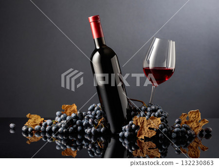 Bottle and glass of red wine with blue grapes on a black background. 132230863