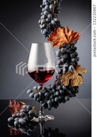 Glass of red wine with blue grapes on a black reflective background. Glass of red wine with blue grapes on a black reflective background. 132230867