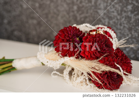 Wedding Bouquet with Red Dahlias and Gold Rings: Romantic Floral Arrangement, Pearl Accents, Dark Background, Ceremony Symbolism, Elegant Still Life. Wedding Bouquet with Red Dahlias and Gold Rings: Romantic Floral Arrangement, Pearl Accents, Dark Background, Ceremony Symbolism, Elegant Still Life. 132231026