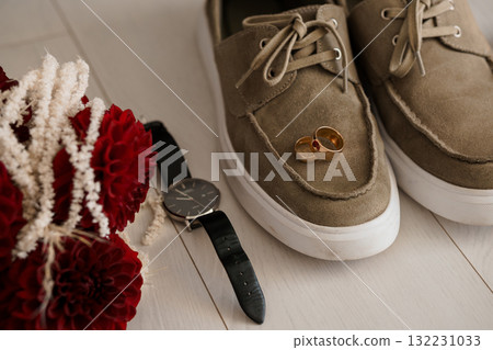Wedding Details Flatlay: Rings, Watch, Brown Suede Shoes, Red Flowers, Groom's Accessories, Light Wood Background, Rustic Chic Style 132231033