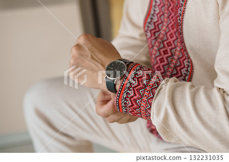 Man Wearing Minimalist Black Watch with Leather Strap and Traditional Embroidered Beige Robe, Close-up, Stylish Accessory, Cultural Fusion. Man Wearing Minimalist Black Watch with Leather Strap and Traditional Embroidered Beige Robe, Close-up, Stylish Accessory, Cultural Fusion. 132231035