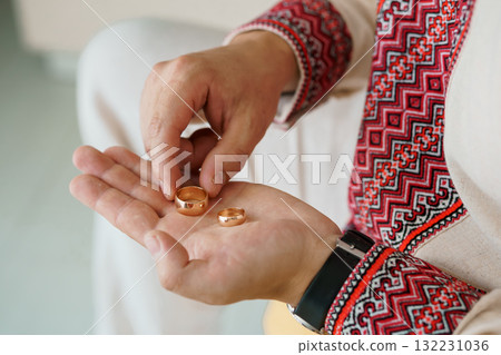 Wedding Rings Exchange Ceremony. Hands Holding Gold Bands. Traditional Ukrainian Vyshyvanka. Red and White Embroidery. Symbolic Love Gesture. Close-up Shot. 132231036