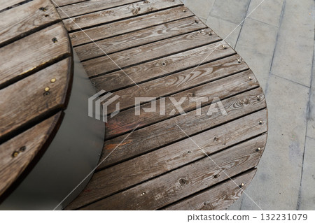 Curved wooden bench rests on gray concrete ground Curved wooden bench rests on gray concrete ground 132231079