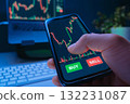A trader holds a smartphone with a stock market trading app on the screen 132231087