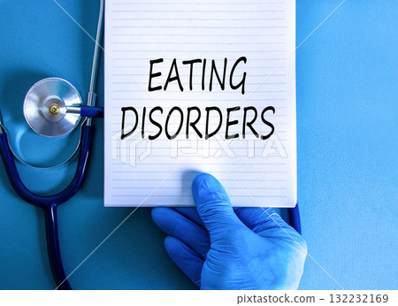Eating disorders symbol. Concept words Eating disorders on beautiful white note. Doctor's hand in blue medical glove. Beautiful blue background. Medical healthy lifestyle eating disorders concept. 132232169