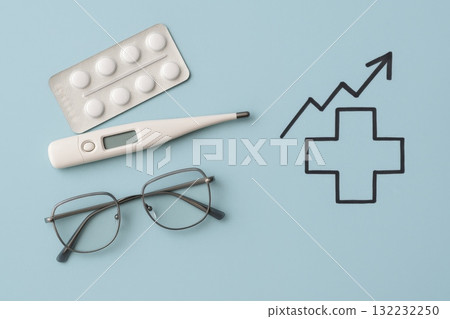 Medical flatlay with thermometer, glasses, pills, and growth chart on blue background 132232250