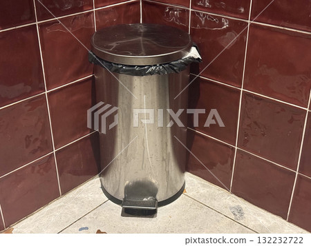 Metal trash bin in restroom corner. Cleanliness, waste management, and hygiene maintenance in everyday public facilities. 132232722