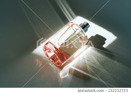Pink perfume bottle on the light background in the rays of sun with highlights. 132232723