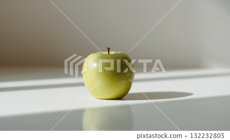 A green apple sits on a table in front of a window 132232805