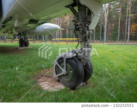 ground level aircraft landing gear showing wheel, strut and hub, grass pad embedment and hydraulic lines visible, maintenance checklist scenario, rugged support feel in outdoor exhibit 132233551