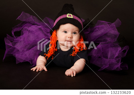 Cute baby in Halloween costume with witch hat and purple tulle skirt on black background 132233620