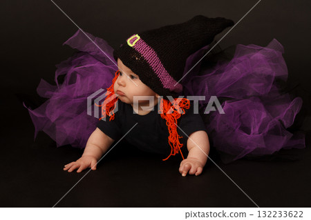 Baby in witch costume with orange yarn hair and purple tulle skirt, looking to the side 132233622