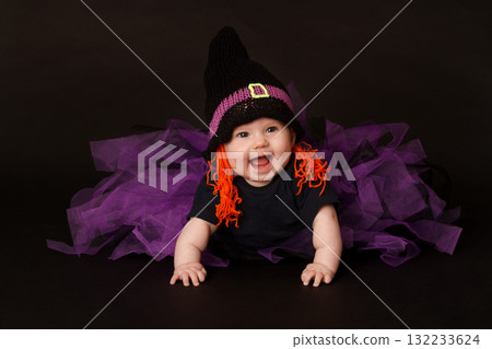 Smiling baby in Halloween witch costume with purple tulle skirt and orange yarn hair 132233624