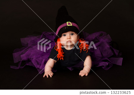 Cute baby in Halloween costume with witch hat and purple tulle skirt on black background 132233625