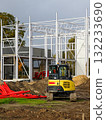 Yellow excavator at modern construction site with steel frame structure and red pipes 132233690