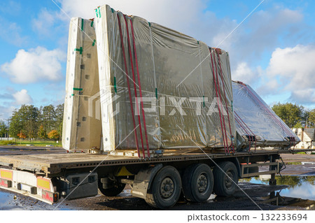 Prefabricated concrete wall panels wrapped in plastic and secured on flatbed truck trailer for transport Prefabricated concrete wall panels wrapped in plastic and secured on flatbed truck trailer for transport 132233694