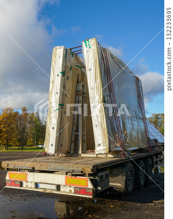 Prefabricated concrete wall panels wrapped and secured on flatbed trailer at construction logistics site Prefabricated concrete wall panels wrapped and secured on flatbed trailer at construction logistics site 132233695