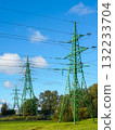 Green electricity pylons with power lines extending across blue sky and rural landscape 132233704